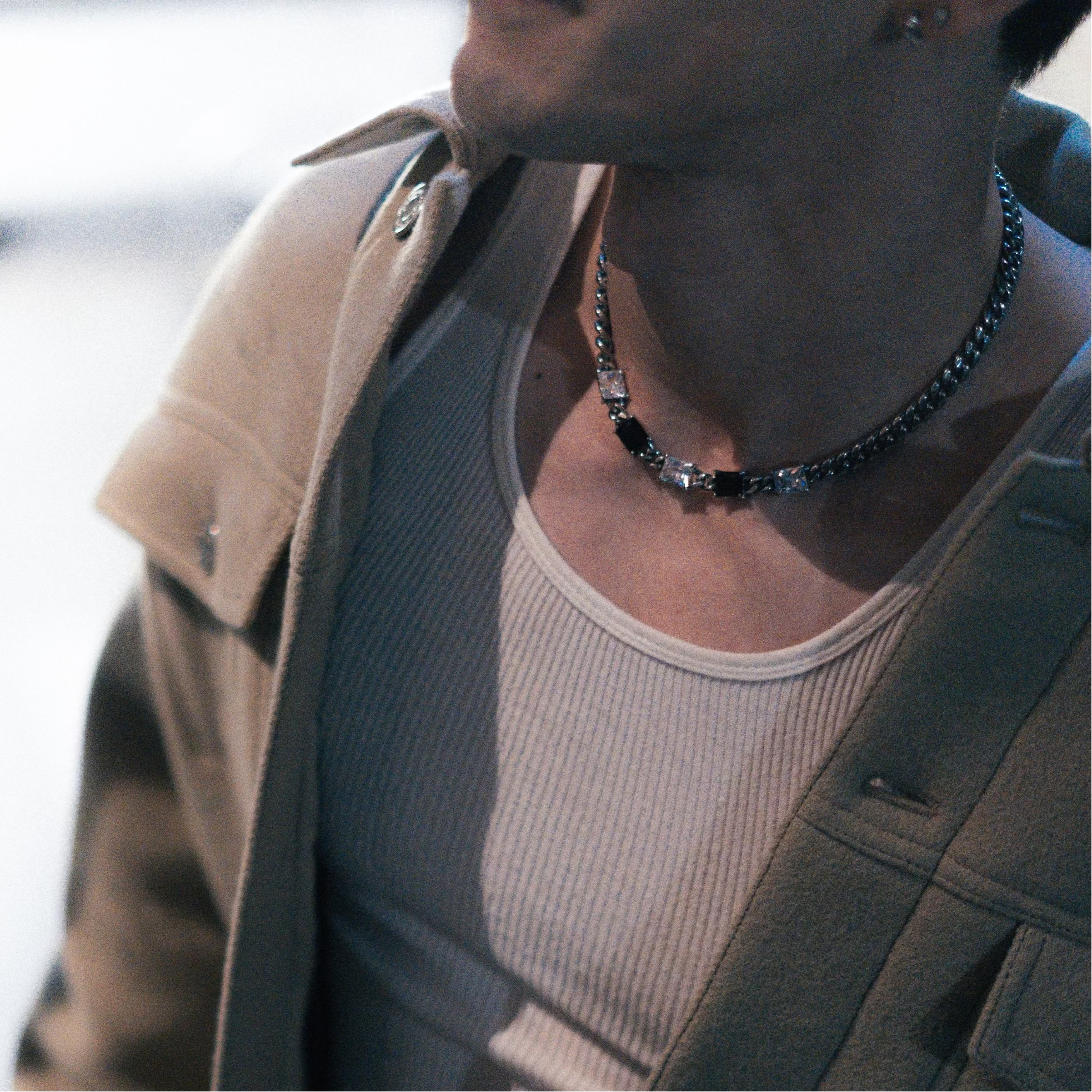 Person wearing a beige jacket over a white shirt with a necklace, blurred background