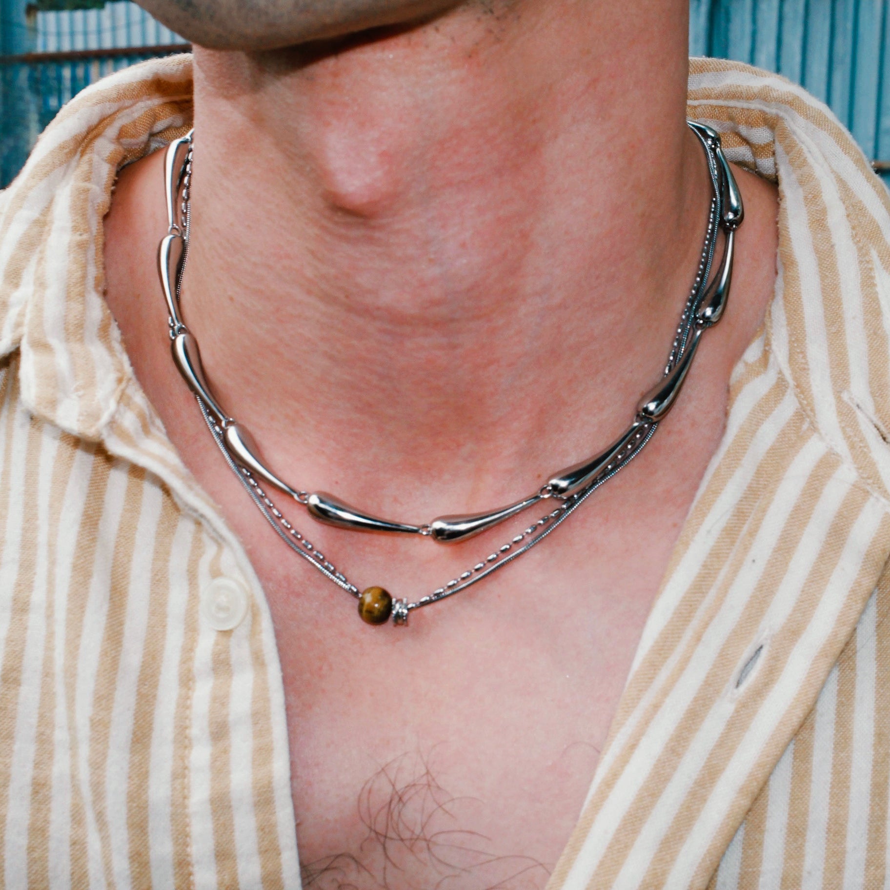 Close-up of a person wearing a silver necklace with a blue background